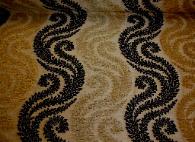 Willoughby Upholstery Fabric in Onyx Embroidered Floral Swirl Pattern in Black and metallic Gold on a tan ground, from Hamilton